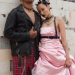 Outdoor Style - Woman in Pink Dress and Man in Black Leather Jacket Standing Beside Brick Wall