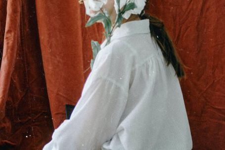 Effortlessly Chic - Side view of unrecognizable young female in elegant clothes sitting in vintage studio and covering face with bunch of delicate white flowers
